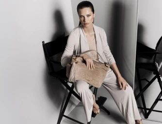 Model Adriana Lima seated on a director chair holding a beige handbag for Donna Karan spring ad campaign.
