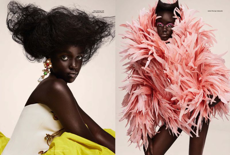 Two dark-skinned fashion models pose against a neutral backdrop; one in a white dress and the other with a feathery pink jacket.