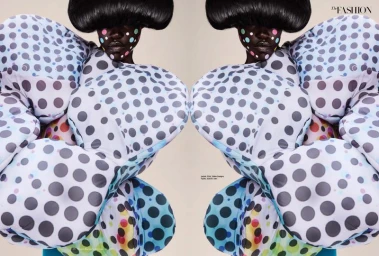 Model wearing a voluminous polka dot padded garment and structured bowl-cut wig with painted facial dots against a neutral background.