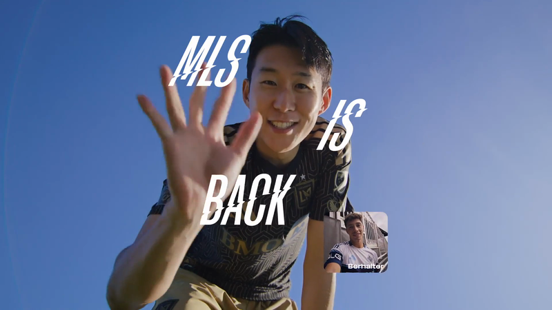 Smiling soccer player waves in front of clear blue sky, overlaid with the text MLS IS BACK, promotional sports content.