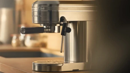 Stainless steel KitchenAid Artisan espresso machine standing on a wooden countertop in a warm interior