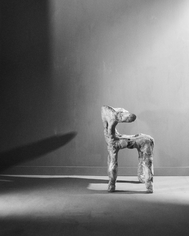 Abstract sculptural chair with rough texture in a dimly lit room. Black and white design evokes art and interior decor.
