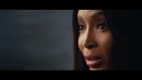 Close-up portrait of Naomi Campbell with dark hair and defined makeup against a dark background for Maybelline