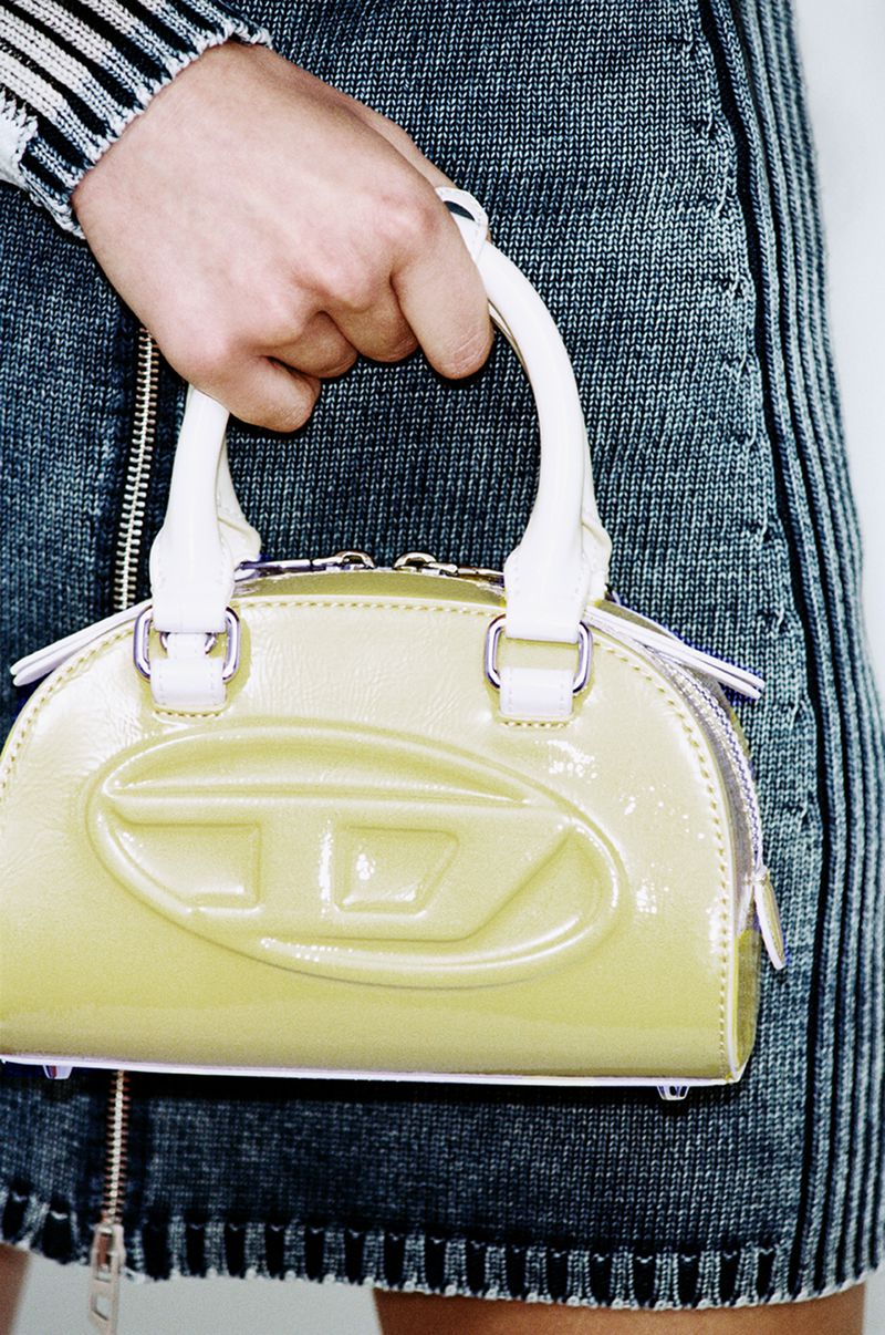 Close-up of a woman holding a patent yellow Diesel logo handbag with white handles, paired with a striped denim skirt.
