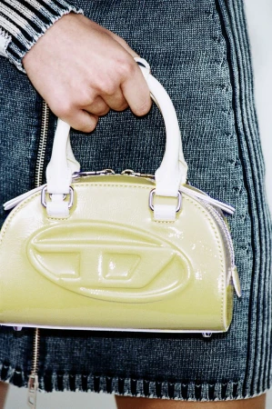 Close-up of a woman holding a patent yellow Diesel logo handbag with white handles, paired with a striped denim skirt.