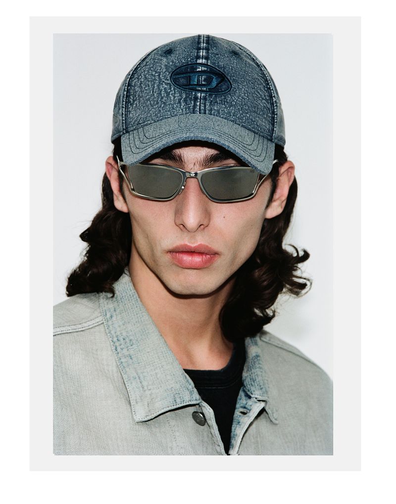 Close-up of a young adult with sunglasses and a denim cap in a studio setting, showcasing a modern casual fashion look.