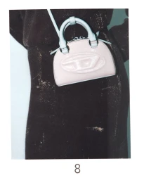 Close-up of a light pink handbag with a embossed D logo worn crossbody against a dark distressed garment.