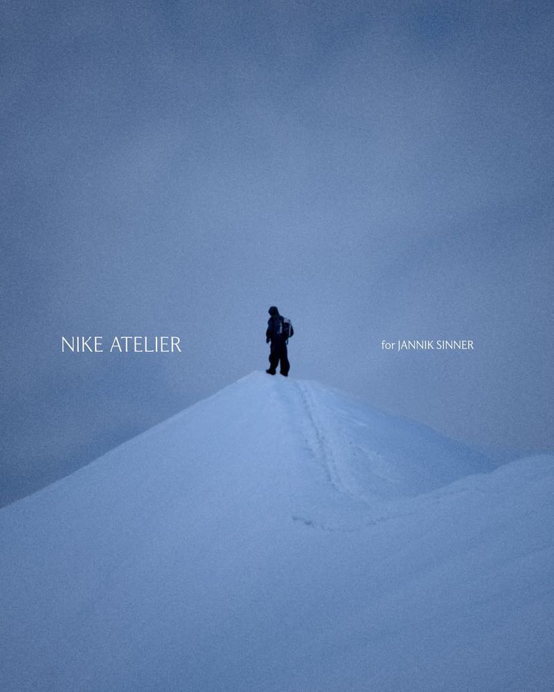 Person in winter clothing stands on a snow-covered mountain peak under a hazy blue sky, promoting Nike Atelier for Jannik Sinner.