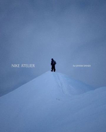 Person in winter clothing stands on a snow-covered mountain peak under a hazy blue sky, promoting Nike Atelier for Jannik Sinner.