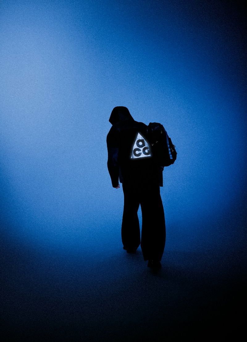Silhouette of a person wearing a hooded jacket with a luminous triangular logo on the back against a blue gradient background