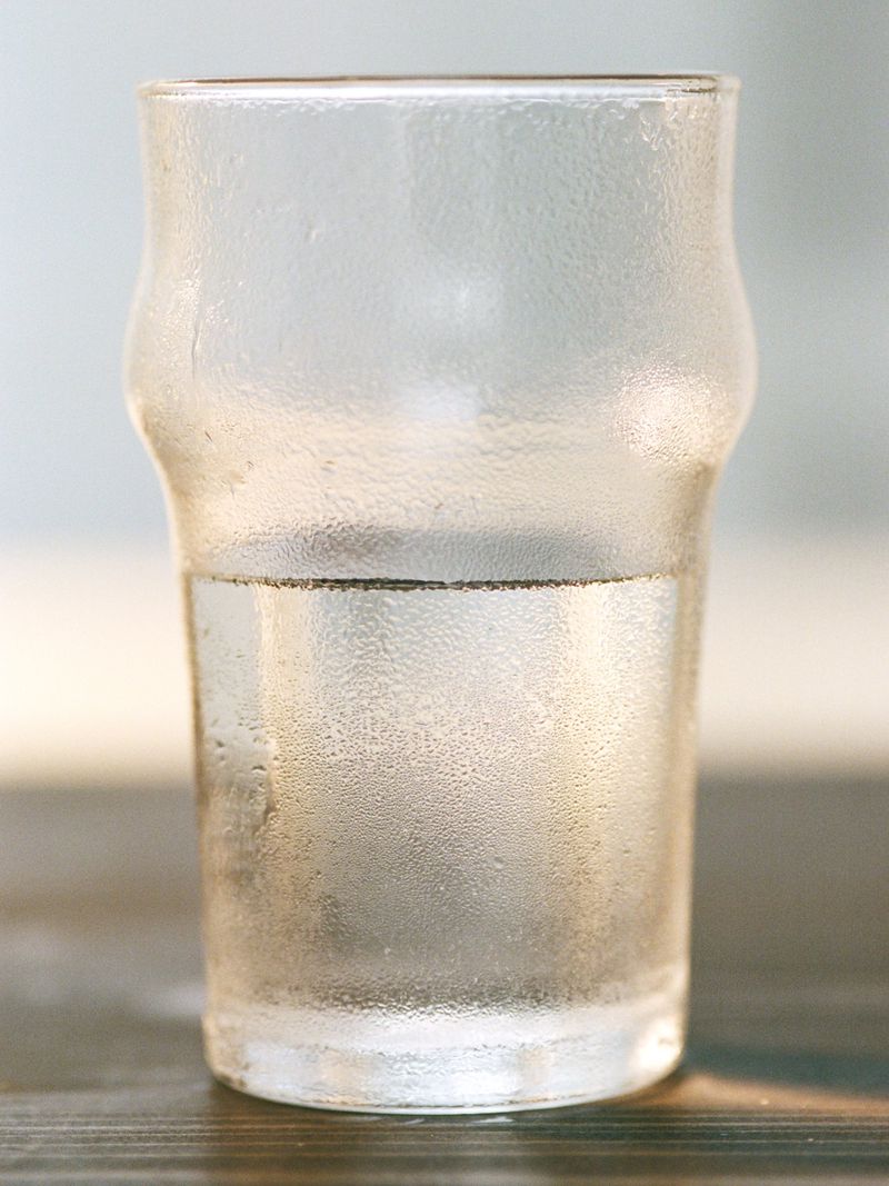 Close-up of a clear glass filled halfway with water, condensation on the glass, and a dark wood surface, clean and crisp.