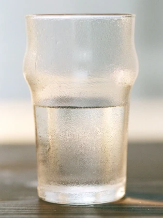 Close-up of a clear glass filled halfway with water, condensation on the glass, and a dark wood surface, clean and crisp.