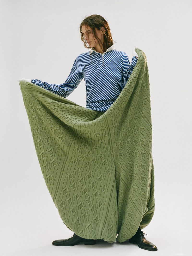 A person in a striped shirt and large green textured pants stands against a white background, showcasing a unique fashion style.