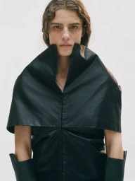 Model wearing a black high collar garment with long sleeves against a solid white background