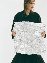 Model wearing a black jacket holding a crumpled sheet of foil in a studio setting