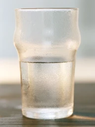 A condensation-covered glass of water resting on a dark surface against a light background