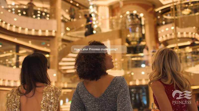 Three women in evening wear are on a cruise ship with multi-level railings and stairs. The cruise line's logo appears on a dress.