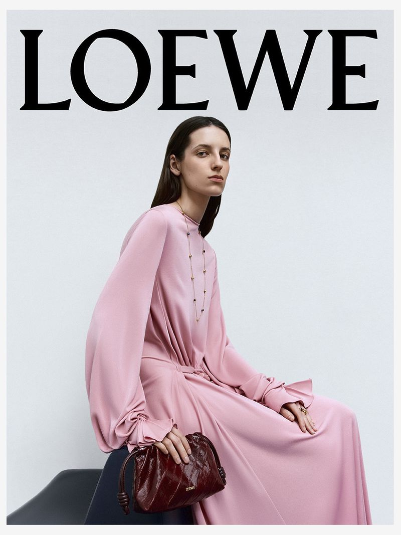 A fashion shot features a slender adult female model in a flowing pink dress, seated and holding a small burgundy leather purse.