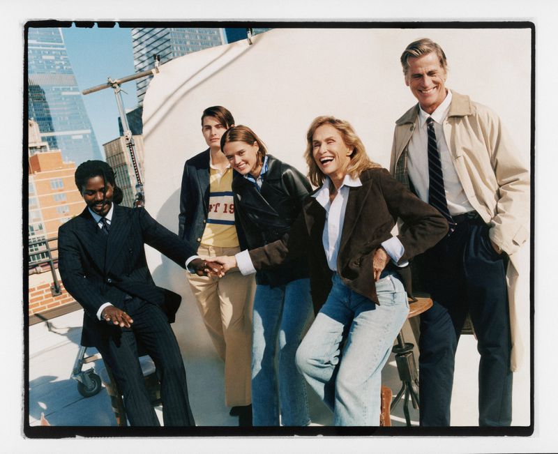 Group of five adult fashion models in casual wear, posing on a rooftop with a city skyline backdrop on a sunny day.