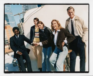 Group of five diverse models smiling on a rooftop photoshoot set against an urban city skyline backdrop.
