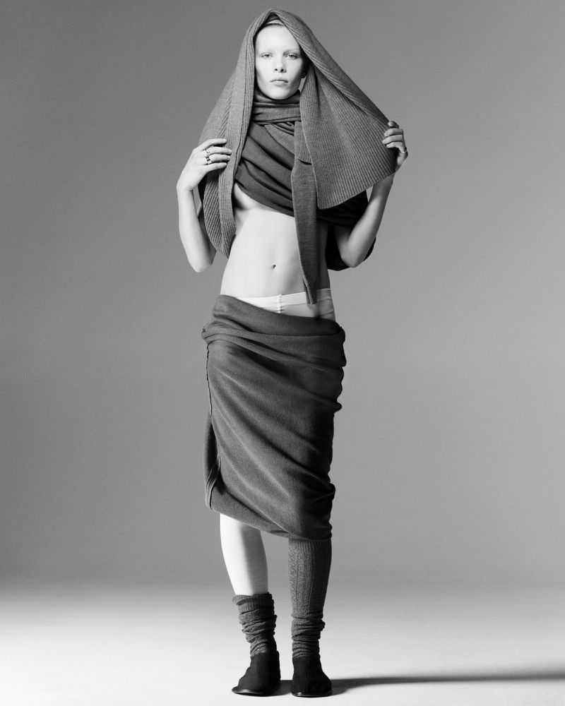 Black and white fashion shot of a slender model with a scarf wrapped around their head and torso, and draped around their waist.