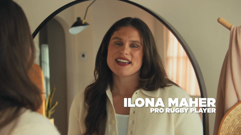 Portrait of Ilona Maher, a pro rugby player, standing indoors, facing the camera, with a mirror and neutral-toned decor in the background.