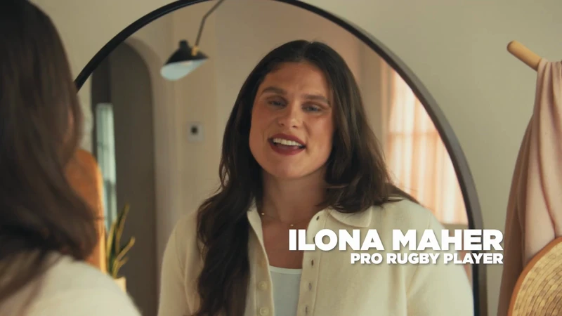 Portrait of Ilona Maher, a pro rugby player, standing indoors, facing the camera, with a mirror and neutral-toned decor in the background.