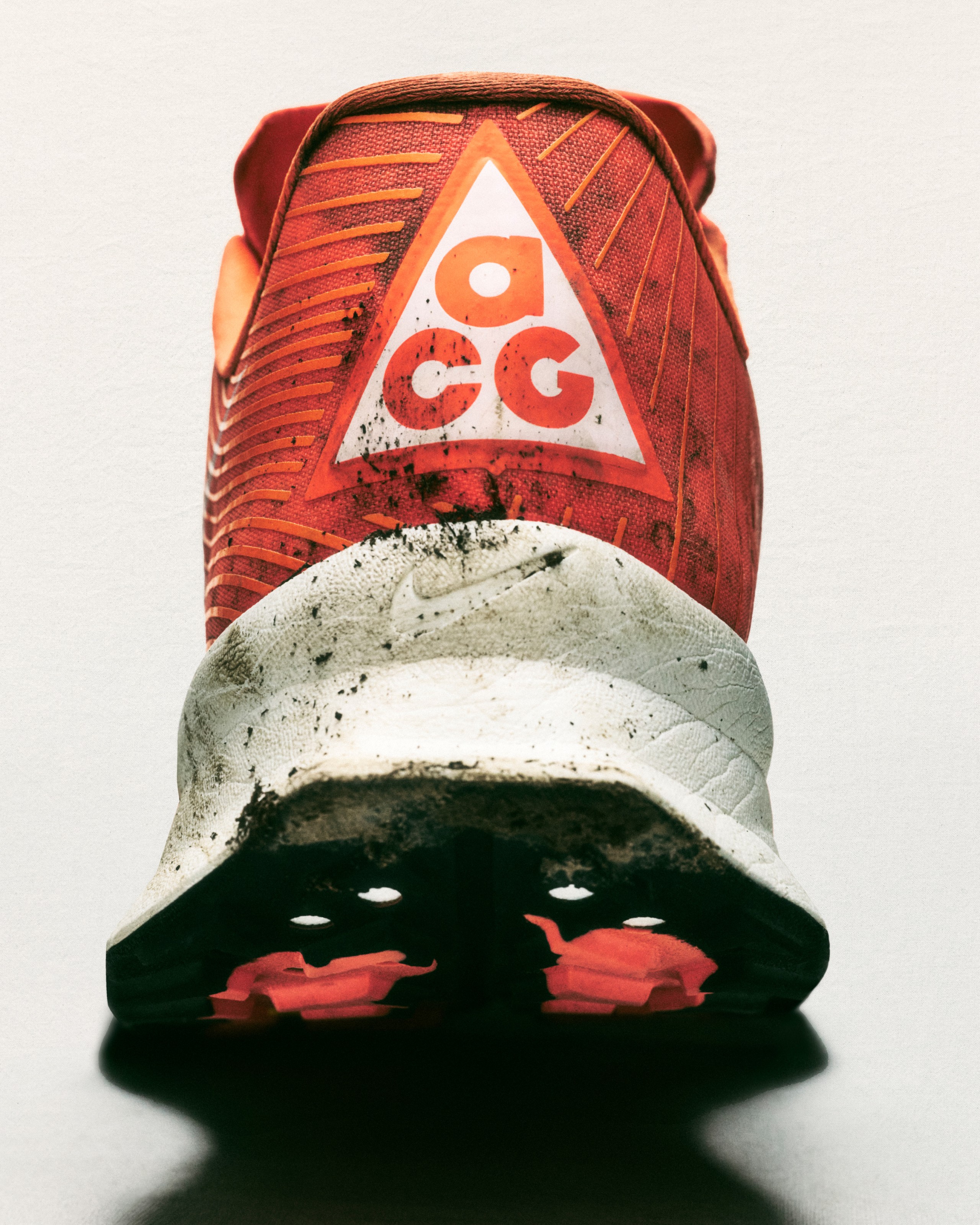 Close-up of a single, dirty orange and white Nike ACG trail running shoe with the sole facing the camera on a white studio background.