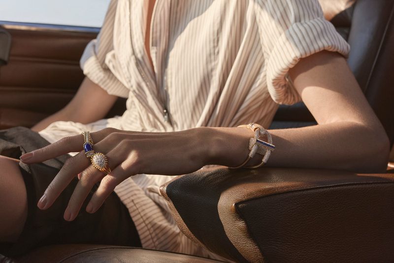 Close-up of a woman's hands adorned with gold rings and a bracelet, showcasing fine jewelry and fashion, against a blurred backdrop.