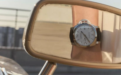 Close-up of a luxury wristwatch reflected in a vehicle side mirror with an out-of-focus urban background