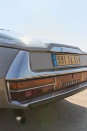Close-up rear view of a vintage car with a yellow license plate under bright daylight.
