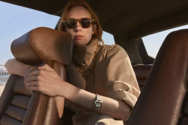 Model wearing sunglasses and a camel coat seated inside a car interior