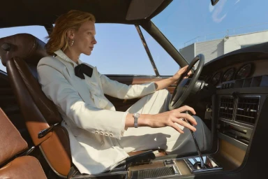 Model Annely Bouma wearing a white suit jacket sitting inside a vintage car for Madame Figaro