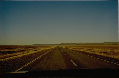 Straight asphalt road stretching across an expansive flat landscape under a clear sky.