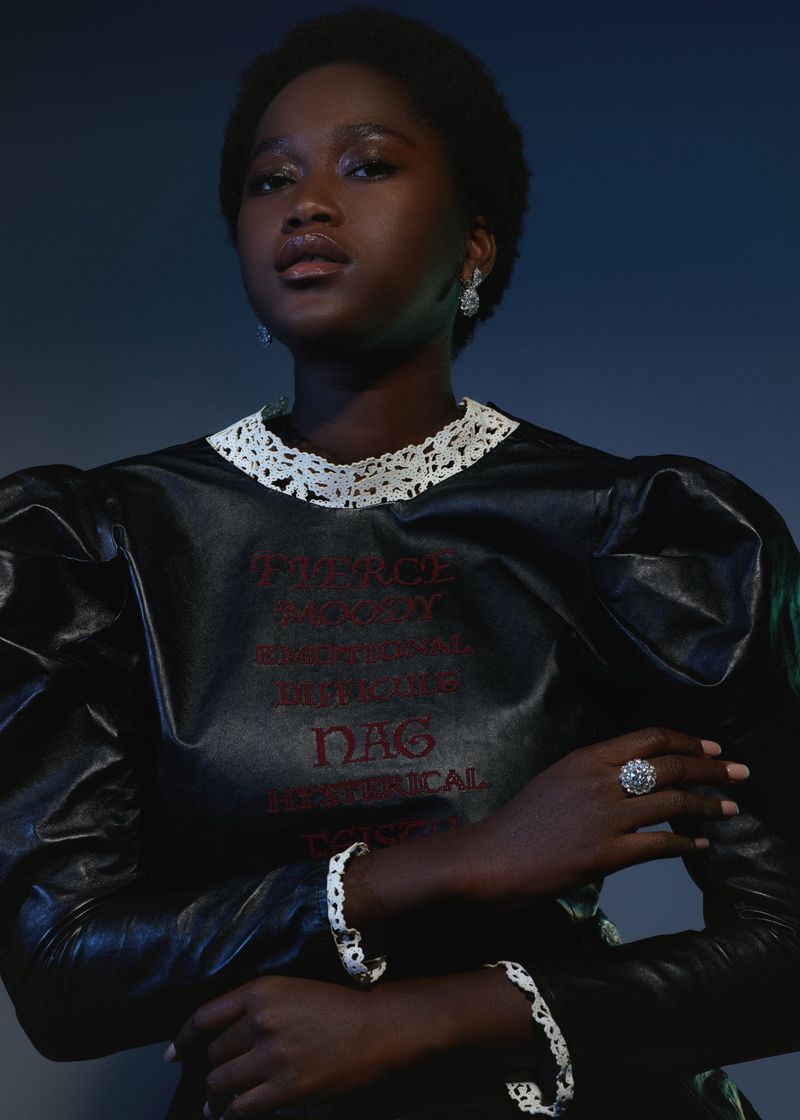 Portrait of a Black woman in a black leather dress with white trim and text, complemented by jewelry against a dark blue background.