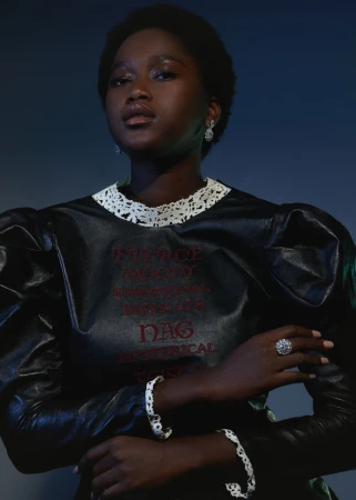 Portrait of a black woman wearing a dark puff sleeve dress with a white lace collar and embroidered red text.