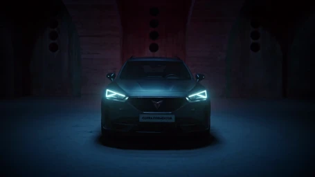 Front view of a dark grey Cupra Formentor SUV parked inside a dimly lit industrial brick tunnel with illuminated headlights.