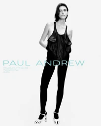 Model wearing dark sleeveless top and black trousers standing against plain white background in Paul Andrew campaign
