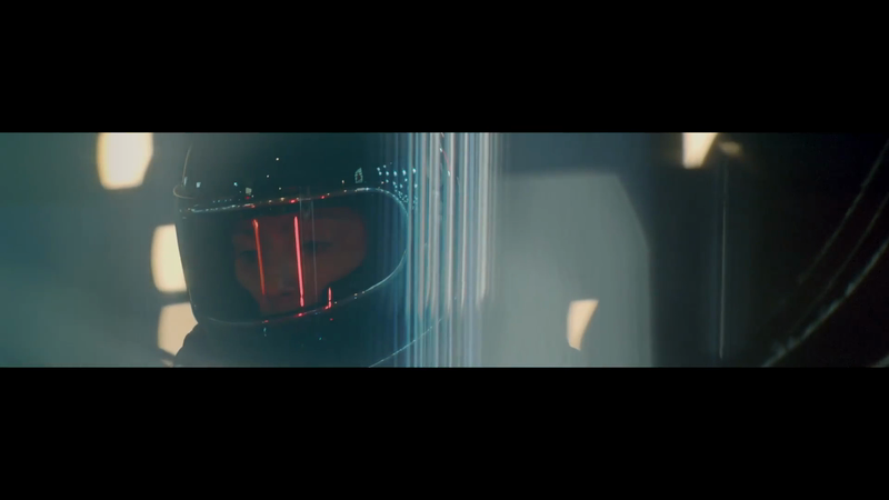 Close-up of adult wearing a dark helmet with visible red lights inside, in front of vertical light pillars in an indoor setting.