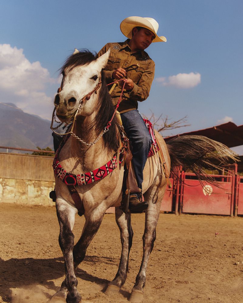 A cowboy riding a horse in an outdoor arena under a bright blue sky, showcasing western riding attire and traditional ranching lifestyle.