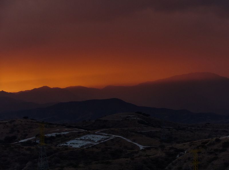 Panoramic view of a mountain range at sunset with orange and purple sky gradient and rolling hills in the foreground.