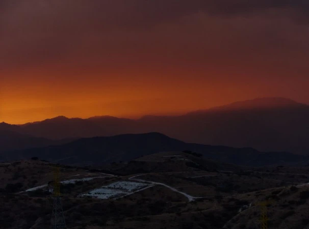 Panoramic view of a mountain range at sunset with orange and purple sky gradient and rolling hills in the foreground.