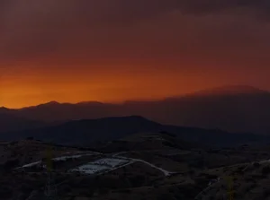 Panoramic landscape view of rolling hills and distant mountains under a dramatic fiery sunset sky by Vivek Vadoliya.