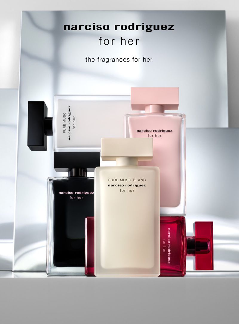 Narciso Rodriguez fragrance bottles in a stack on a reflective surface. Different colored bottles including black, pink, red, and cream.