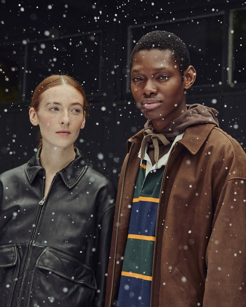 Portrait of a Black male and a redhead female wearing winter coats in a studio setting with digitally added snow effect.