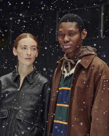 Portrait of a Black male and a redhead female wearing winter coats in a studio setting with digitally added snow effect.