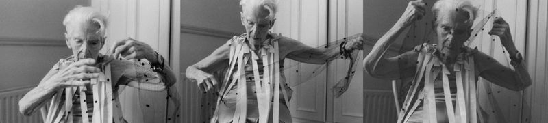 Monochrome triptych shows an older person with short white hair indoors, wearing a light-colored garment with dark dots and white stripes.
