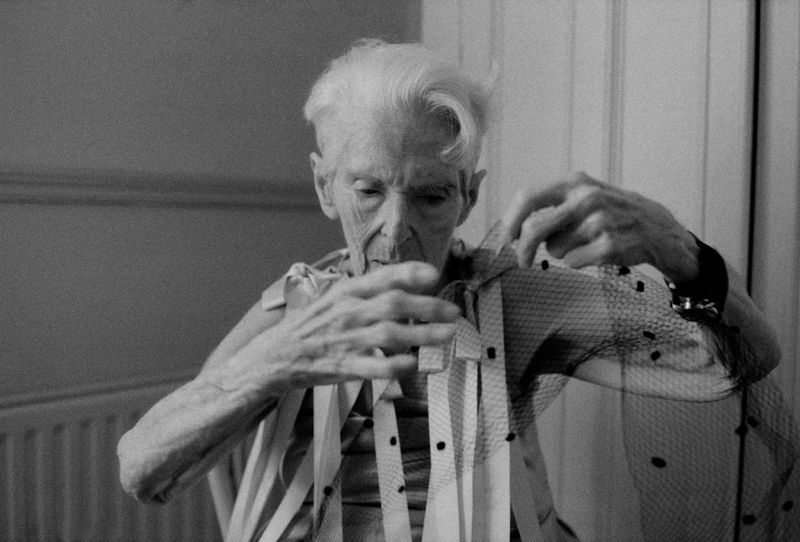 Elderly woman indoors in black and white. Holding netting material with polka dot pattern and wearing striped top in an indoor setting.