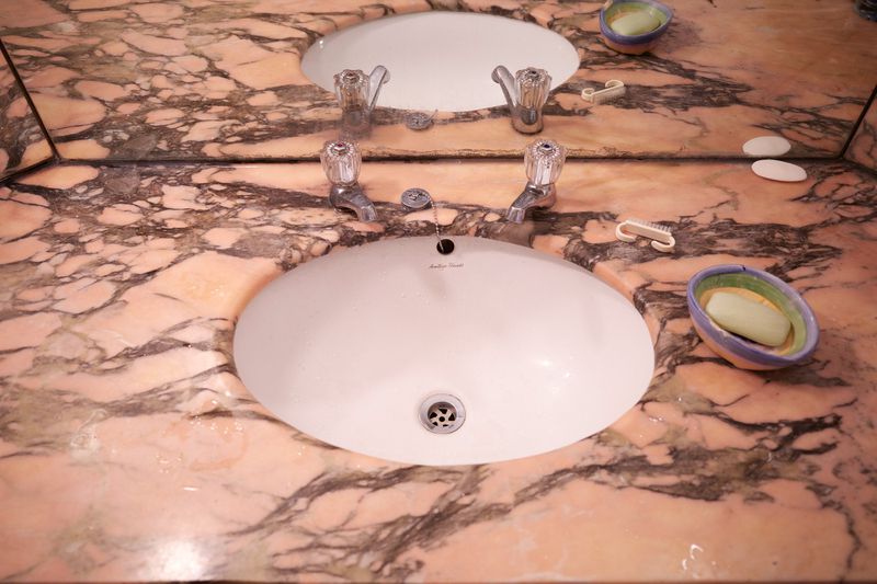 Elevated angle captures a bathroom vanity with a double sink, featuring marble countertops, chrome faucets, and personal hygiene items.