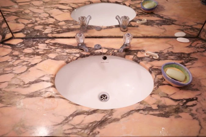 Elevated angle captures a bathroom vanity with a double sink, featuring marble countertops, chrome faucets, and personal hygiene items.